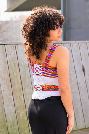 Back of woman wearing a Latin-inspired,white colorful striped corset top with 2 inch straps, made with Peruvian Aguayo fabric