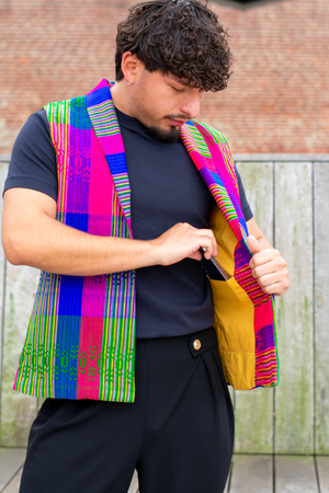 Model wearing a Latin-inspired, artisan-made, semi-fitted, colorful vest handwoven in El Salvador with a collar over a black shirt. 