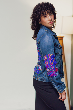Person wearing a blue denim jacket with colorful elbow patches.