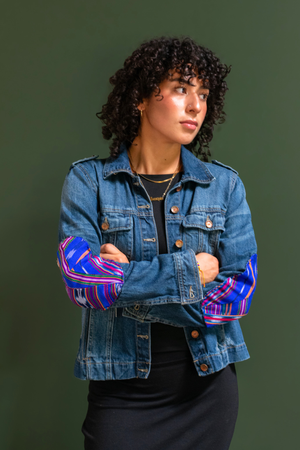 Person wearing a denim jacket with colorful sleeves against a green background