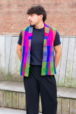 Model wearing a Latin-inspired, artisan-made, semi-fitted, colorful vest handwoven in El Salvador with a collar over a black crewneck shirt 