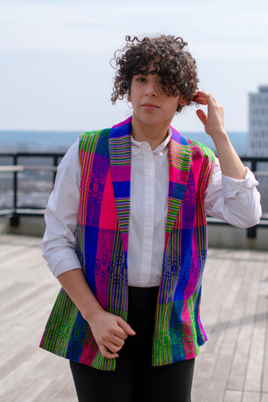 Model wearing a Latin-inspired, artisan-made, semi-fitted, colorful vest handwoven in El Salvador with a collar over a white button-up shirt. 