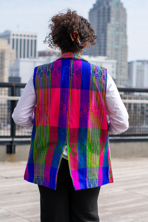 Back of a model wearing a Latin-inspired, artisan-made, semi-fitted, colorful vest handwoven in El Salvador with a collar over a white button-up shirt. 