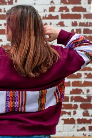 Close up of the back of a woman wearing a Latin-inspired, ethically-made, oversized, burgundy sweater with colorful patterned sleeves made with Aguayo fabric from Peru